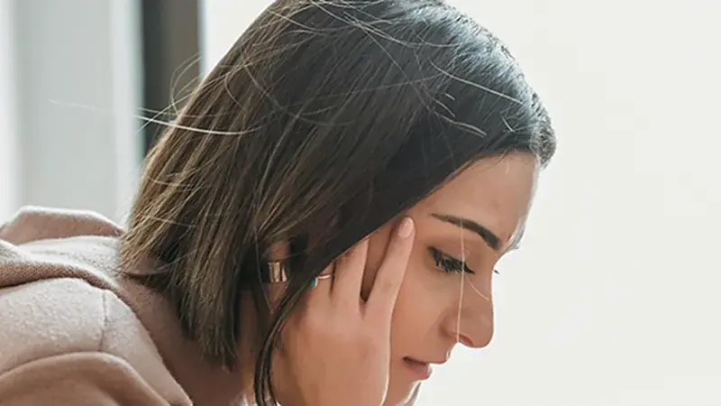 Woman holding her head, experiencing a migraine